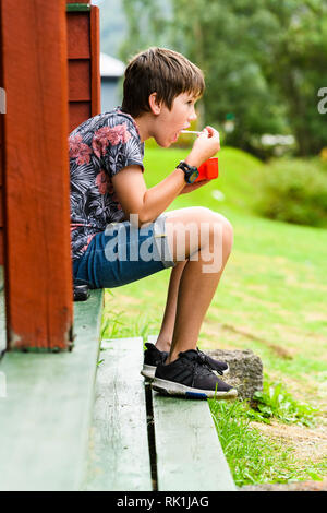 Portrait der Junge sitzt außerhalb Holzhütte, zu frühstücken. Flam, Norwegen, Europa Stockfoto