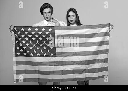 Paar auf ruhige Flächen hält Flagge der USA. Paar begrüßt die USA zu besuchen. Guy und Mädchen stolz, Amerikaner zu sein, grauen Hintergrund. Language School Konzept. Stockfoto