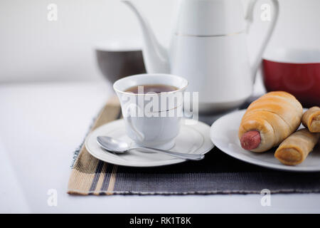 Tea time - ein Schuss eines weißen Teller mit Gebäck, eine Teekanne und Tasse auf einem schwarzen Tischplatte, farbige Tassen und Tabelle mat Stockfoto