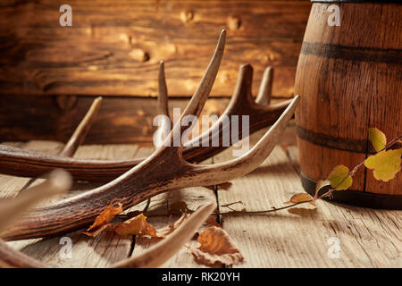 Rustikale Hunter House oder bar Dekoration von Deer Antler, Herbst gelbe Blätter und Holzfass auf der Oberfläche der alten Holztisch Stockfoto