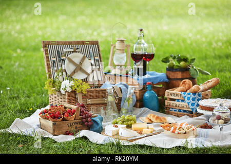 Wicker Picknick mit sortierten frische Lebensmittel, Wasser und Wein auf eine Wolldecke ausgebreitet auf dem grünen Rasen in einem Park behindern Stockfoto