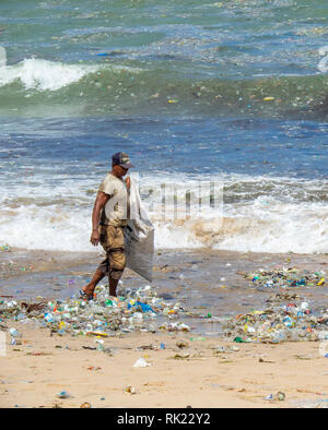 Umweltverschmutzung, einsame Mann herauf Kunststoff Flaschen, Becher, Strohhalme und sonstigem Abfall bis auf den Strand gespült an der Jimbaran Bay, Bali Indonesien.. Stockfoto