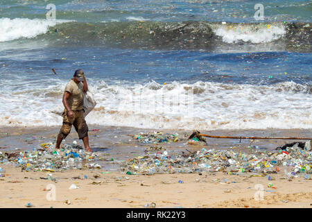 Umweltverschmutzung, einsame Mann herauf Kunststoff Flaschen, Becher, Strohhalme und sonstigem Abfall bis auf den Strand gespült an der Jimbaran Bay, Bali Indonesien.. Stockfoto