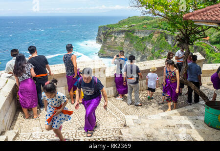 Chinesische Touristen tragen lila Sarongs besuchen Uluwatu Tempel Bali Indonesien. Stockfoto