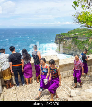 Chinesische Touristen tragen lila Sarongs besuchen Uluwatu Tempel Bali Indonesien. Stockfoto