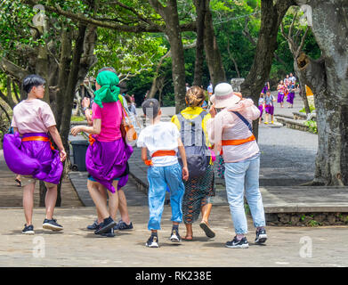 Chinesische Touristen tragen lila Sarongs besuchen Uluwatu Tempel Bali Indonesien. Stockfoto