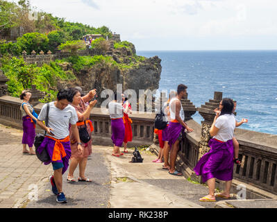 Chinesische Touristen tragen lila Sarongs besuchen Uluwatu Tempel Bali Indonesien. Stockfoto