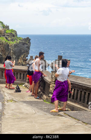 Chinesische Touristen tragen lila Sarongs besuchen Uluwatu Tempel Bali Indonesien. Stockfoto