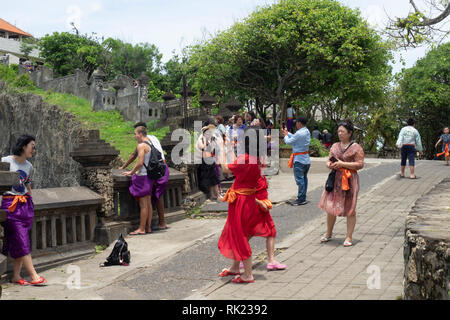 Chinesische Touristen tragen lila Sarongs besuchen Uluwatu Tempel Bali Indonesien. Stockfoto