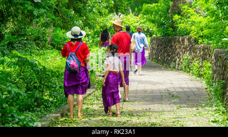 Chinesische Touristen tragen lila Sarongs besuchen Uluwatu Tempel Bali Indonesien. Stockfoto