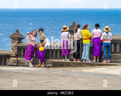 Chinesische Touristen tragen lila Sarongs besuchen Uluwatu Tempel Bali Indonesien. Stockfoto