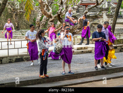 Chinesische Touristen tragen lila Sarongs besuchen Uluwatu Tempel Bali Indonesien. Stockfoto