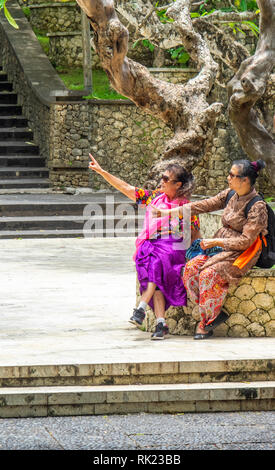 Chinesische Touristen tragen lila Sarongs besuchen Uluwatu Tempel Bali Indonesien. Stockfoto