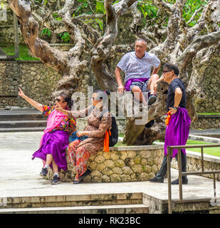 Chinesische Touristen tragen lila Sarongs besuchen Uluwatu Tempel Bali Indonesien. Stockfoto