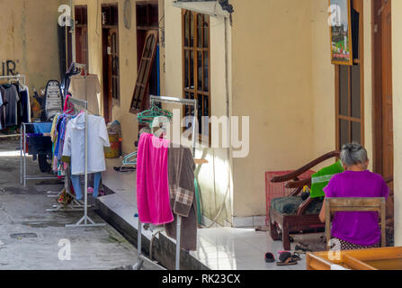 Dame auf der Veranda von Regalen gebügelte Kleidung und Handtücher, Jimbaran, Bali Indonesien umgeben. Stockfoto