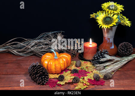 Seide Ahornblätter, schönen Blumenstrauß aus Sonnenblumen, mattierte Kiefernzapfen und orange Kerze auf der Tischplatte mit dunklem Hintergrund. Stockfoto