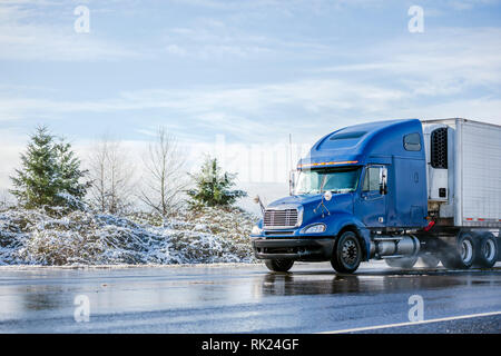 Big Rig pro Long Haul blue Semi Truck Traktor Transport von kommerziellen Ladung im Kühlschrank Auflieger gehen auf das Nass glänzende Straße mit Wasser aus Stockfoto