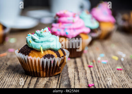 Chocolate Cupcake mit farbigen Rosa und grün Creme auf Holz Tisch Stockfoto