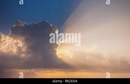 Schöne lebendige Morgen blauer Himmel Hintergrund mit weichen langen goldenen Sonnenstrahlen hinter weißen flauschigen Wolke draußen scheint. Horizontale Farbfotografie. Stockfoto