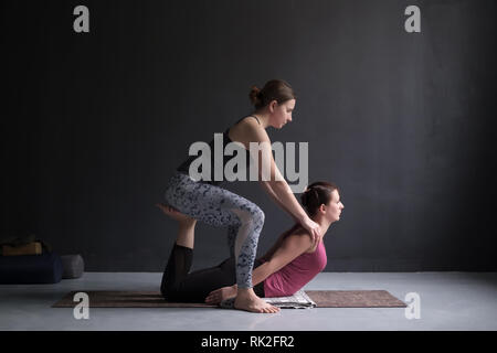Sportliche yoga Mädchen helfen, ihr Freund zu bhudjangasana oder Kobra tun Stockfoto