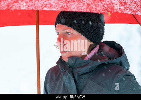 Traurig, enttäuscht, Frau im Stehen im Winter Schnee unter großen roten Regenschirm Stockfoto