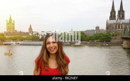 Glücklich lächelnde Frau, die ihre Reisen in Deutschland genießen. Schöne traveler Girl vor der Kamera mit dem Kölner Dom und der Rhein o Posing Stockfoto