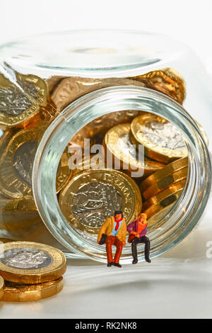 Konzeptionelle diorama Bild von miniaturfiguren saß auf einem Glas Glas mit Pfund Münzen gefüllt Stockfoto