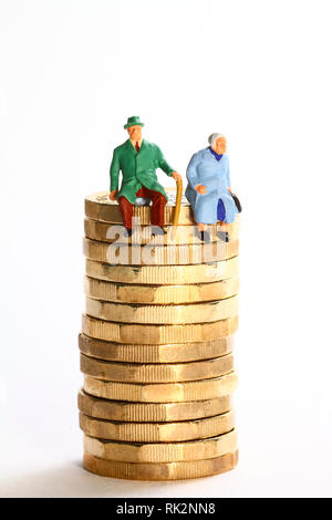 Konzeptionelles Diorama-Bild einer Miniaturfigur Rentnerpaar saß Auf einem Stapel von Pfund-Münzen Stockfoto