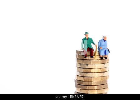 Konzeptionelles Diorama-Bild einer Miniaturfigur Rentnerpaar saß Auf einem Stapel von Pfund-Münzen Stockfoto