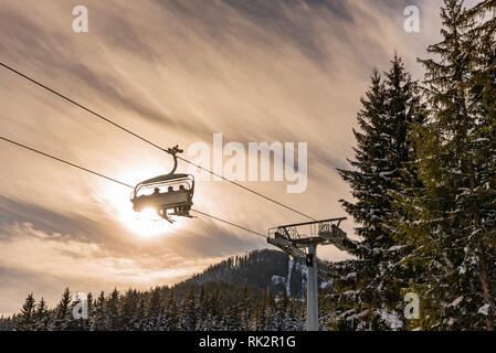 Vier Skifahrer auf einem Sessellift vor dem Hintergrund der Sonne und Bäume, Kontur Foto, orange Farbtöne, Skigebiet Schladming Österreich Stockfoto