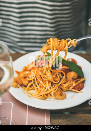 Italienisches Abendessen im Bistrot mit spaghetti Pasta mit Garnelen und Glas Weisswein. Mann essen Nudeln mit Gabel. Köstliche italienische Küche Konzept Stockfoto