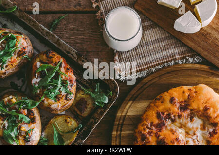 Gebackene gefüllte Kartoffeln mit Käse, Gemüse, Sauerrahm und Rucola auf hölzernen Tisch. Ansicht von oben Stockfoto