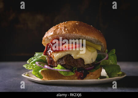 Nahaufnahme von hausgemachten Classic Burger in Weizen Brötchen mit Rind- und Kalbfleisch Schnitzel, geschmolzenem Käse und Gemüse auf weißer Keramik Platte über dunkle Tabelle. Kopieren Stockfoto