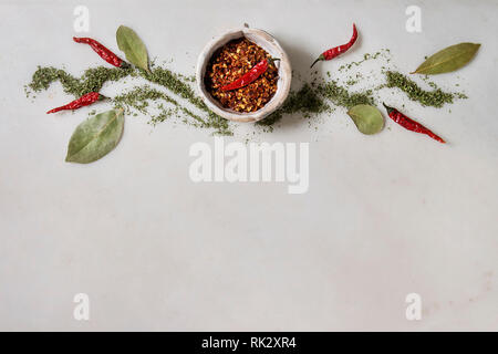 Gewürze und Kräuter. Red Hot Chili Pepper Flakes in Keramik Schüssel mit Lorbeerblatt und Minze Dekor in weißem Marmor Hintergrund. Flach, Platz. Kochen conc Stockfoto
