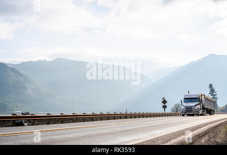 Big Rig Low cab wirtschaftlich lange Motorhaube Semi Truck Transport von kommerziellen Ladung im abgedeckten bulk Auflieger, die auf der schmalen Straße entlang der Stockfoto