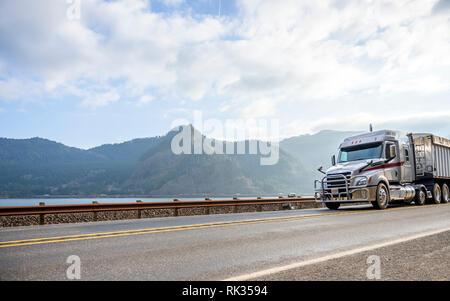 Big Rig Low cab wirtschaftlich lange Motorhaube Semi Truck Transport von kommerziellen Ladung im abgedeckten bulk Auflieger, die auf der schmalen Straße entlang der Stockfoto