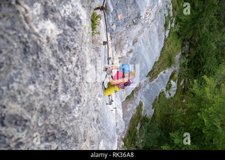 Weibliche Touristen, in bunten Sport Kleidung, klettert eine schwierige vertikalen Abschnitt auf einen Klettersteig Route über Hallstatt, Österreich, während ein Sommer climbi Stockfoto