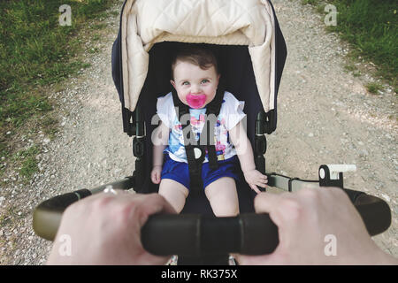 Kleines Mädchen im Kinderwagen sitzen. Hände halten Kinderwagen bewältigen. Stockfoto