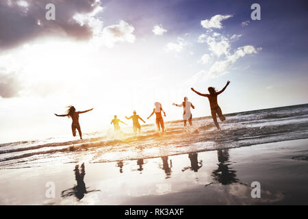 Gruppe der glücklichen Völker läuft und springt bei Sonnenuntergang am Strand. Tropische Tourismus Konzept Stockfoto