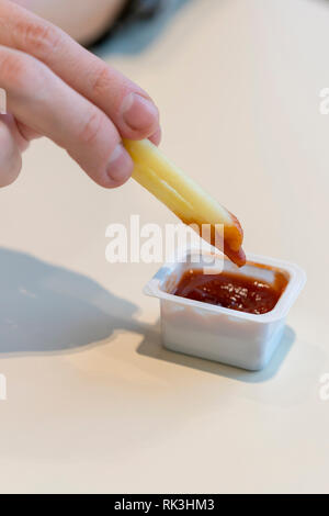 In der Nähe der weiblichen Hand tauchen Pommes in Tomatensoße. Hand mit frischen Pommes Frites tauchte in Tomatensauce. Vertikaler. Kopieren Sie Platz Stockfoto