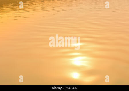 Schönen Sonnenuntergang Wasser Hintergrund. Die Wellen auf der Oberfläche des Flusses. In der Dämmerung Zeiten und Reflexionen. Golden und orange Farben in die Wellen. Stockfoto