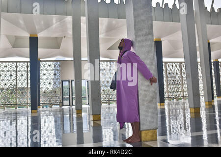 Ein männlicher Tourist in der National Moschee der Stadt Kuala Lumpur steht in der Nähe der Lenksäule und genießt die Schönheit des Inneren. Stockfoto