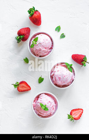 Erdbeereis und frische Erdbeeren auf weißem Hintergrund, Ansicht von oben. Drei Becher Erdbeereis, gesunden Sommer Nachtisch. Stockfoto