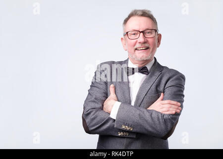 Senior Geschäftsmann in Anzug und Fliege mit verschränkten Armen posing Stockfoto