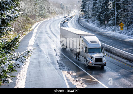 Big Rig Long Haul grau Semi Truck Traktor Transport von kommerziellen Ladung in trockenen van Auflieger gehen auf den nassen rutschigen Straße mit Wasser aus Schmelzen Stockfoto
