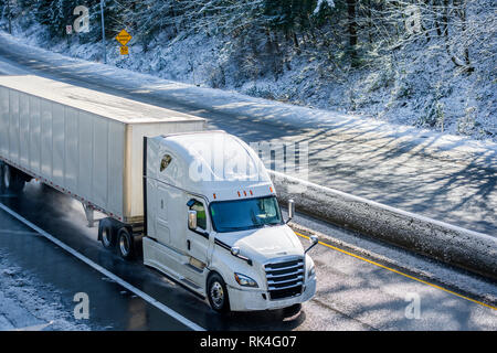 Big Rig Long Haul grau Semi Truck Traktor Transport von kommerziellen Ladung in trockenen van Auflieger gehen auf den nassen rutschigen Straße mit Wasser aus Schmelzen Stockfoto