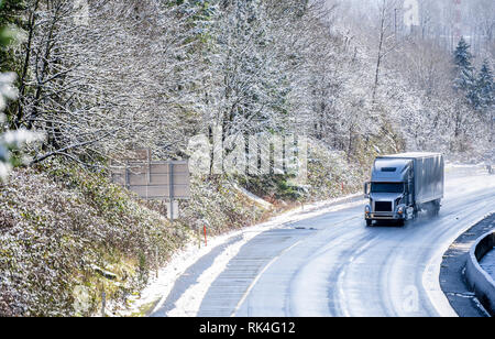Big Rig Long Haul grau Semi Truck Traktor Transport von kommerziellen Ladung in trockenen van Auflieger gehen auf den nassen rutschigen Straße mit Wasser aus Schmelzen Stockfoto