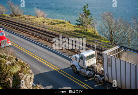 Big Rig Low cab wirtschaftlich lange Motorhaube Semi Truck Transport von kommerziellen Ladung in loser Schüttung Auflieger, die auf der schmalen Straße entlang dem columbi Stockfoto
