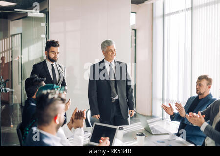 Team verschiedener mittleren Alters multiethnischen männlichen Investoren, die von den älteren im Alter von erfahrenen Regisseur, die Zusammenarbeit bei der Entwicklung gemeinsamer Investitionen proj Stockfoto