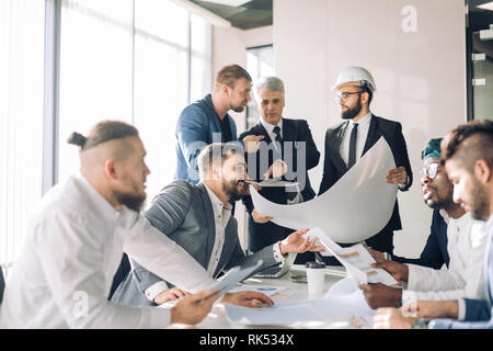 Fokussierte Indischen, Arabischen und kaukasischen Ingenieure, mit einem von ihnen tragen, hardhat, diskutieren Bau Grafiken und Plänen in der Konstruktion compa Stockfoto